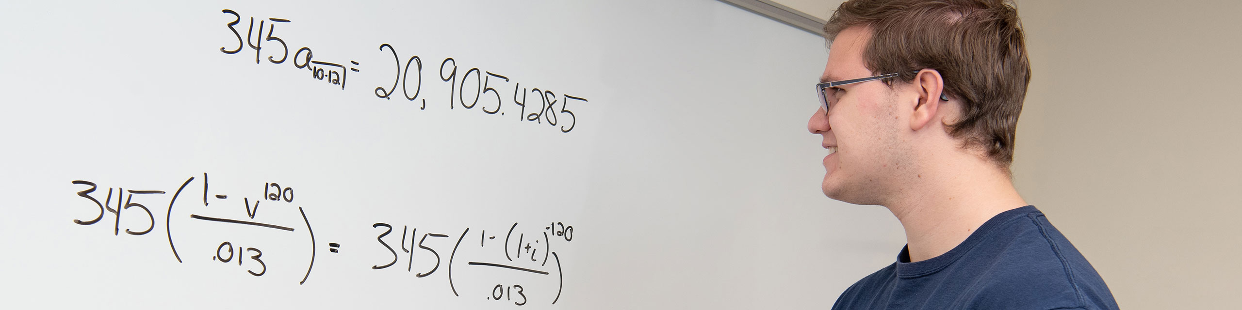 Student looking to a white board with some mathematical expressions written on it.