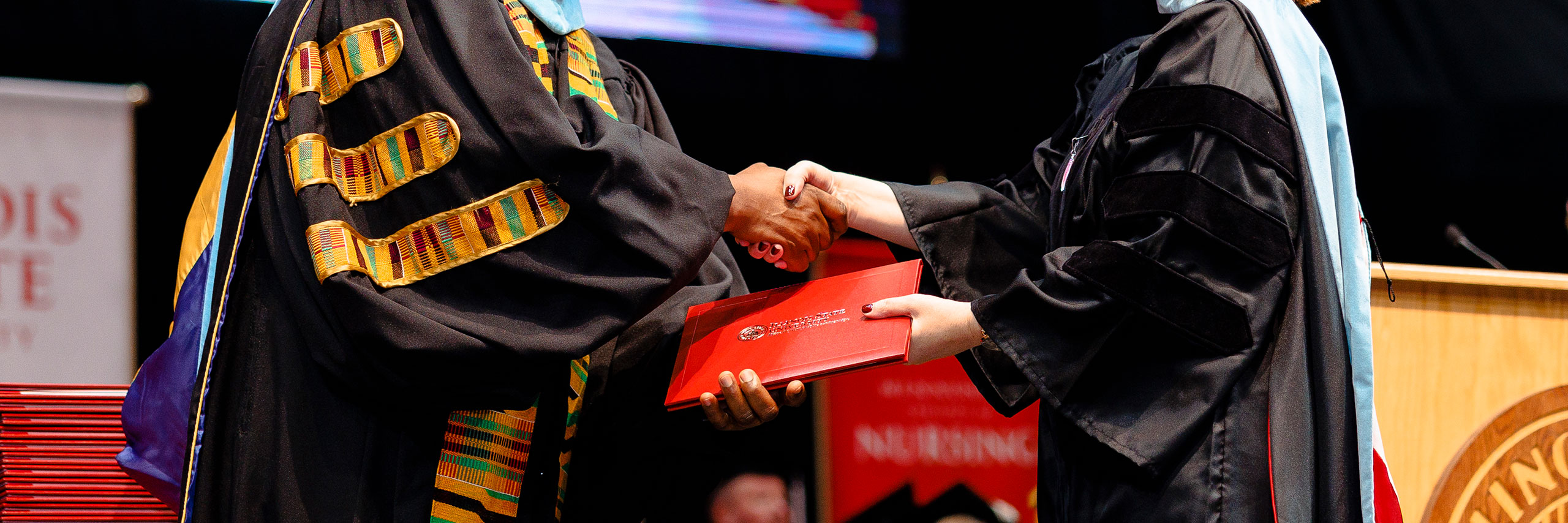 A degree being handed out while a staff and a student shake hands.